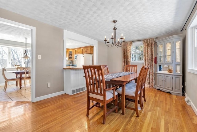 dining room with light wood finished floors, baseboards, a chandelier, and a textured ceiling