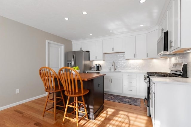 kitchen with a breakfast bar, stainless steel appliances, sink, white cabinets, and light hardwood / wood-style floors