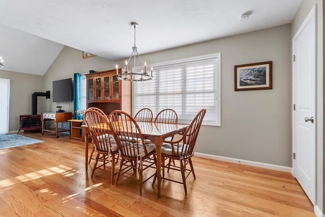 dining space featuring a wood stove, light hardwood / wood-style floors, vaulted ceiling, and a notable chandelier