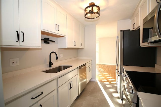 kitchen with white cabinetry, stainless steel appliances, sink, and light stone counters