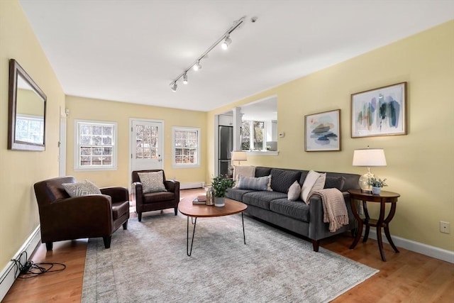 living area featuring a baseboard heating unit, plenty of natural light, wood finished floors, and baseboards