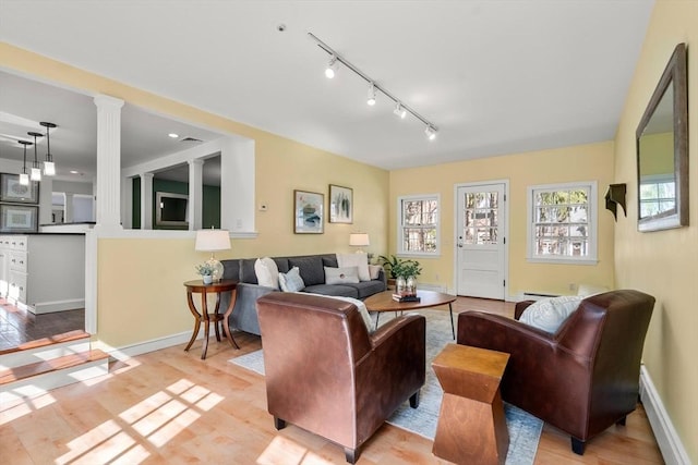 living area with rail lighting, decorative columns, baseboards, and wood finished floors