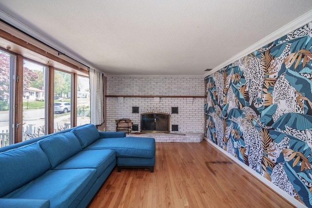 living room featuring a textured ceiling, ornamental molding, wood finished floors, brick wall, and a brick fireplace