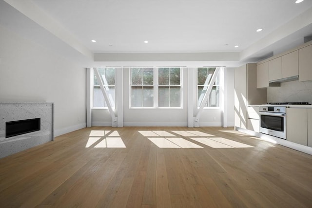 unfurnished living room with a wealth of natural light, a high end fireplace, and light hardwood / wood-style flooring