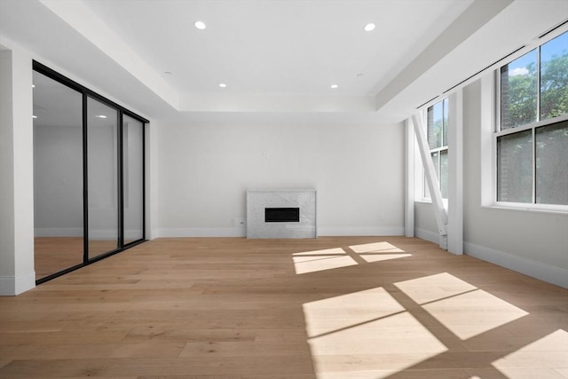 unfurnished living room featuring a raised ceiling, a premium fireplace, and light hardwood / wood-style flooring