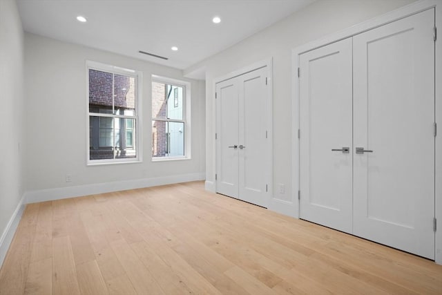 unfurnished bedroom featuring multiple closets and light hardwood / wood-style floors