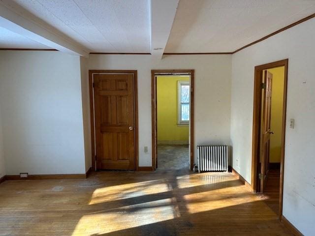 empty room featuring hardwood / wood-style flooring, radiator, and ornamental molding