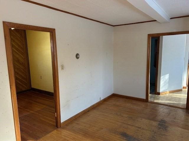 empty room with beam ceiling, wood-type flooring, and ornamental molding