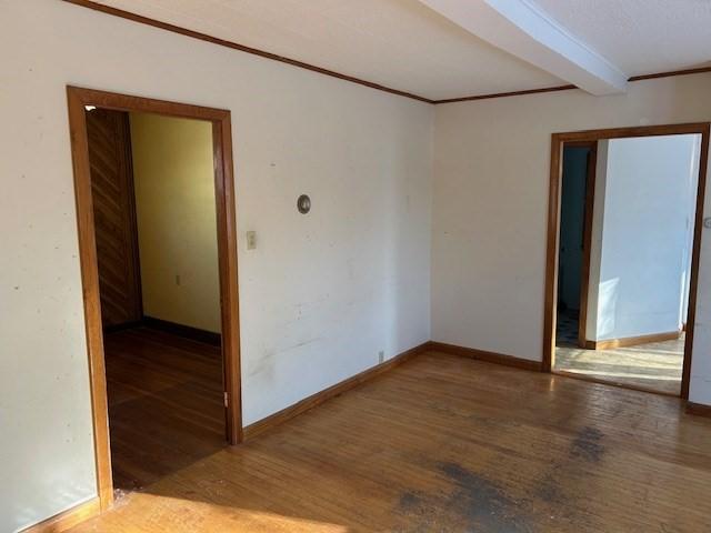 empty room featuring hardwood / wood-style floors, beamed ceiling, and ornamental molding