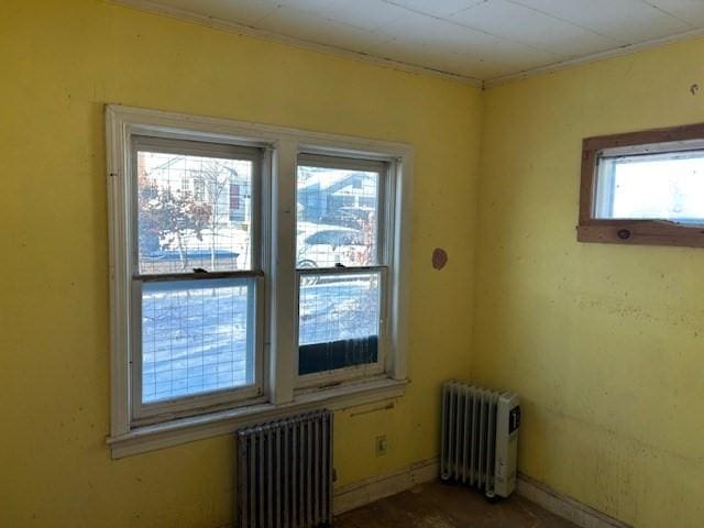 spare room with radiator heating unit, a wealth of natural light, and ornamental molding