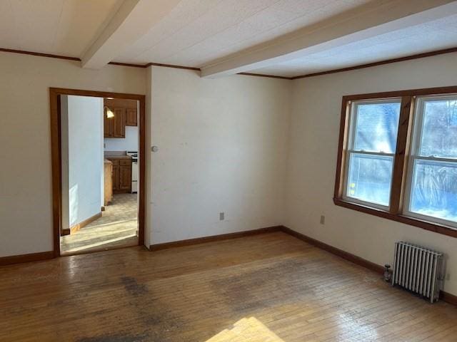 spare room with radiator heating unit, beamed ceiling, and light wood-type flooring