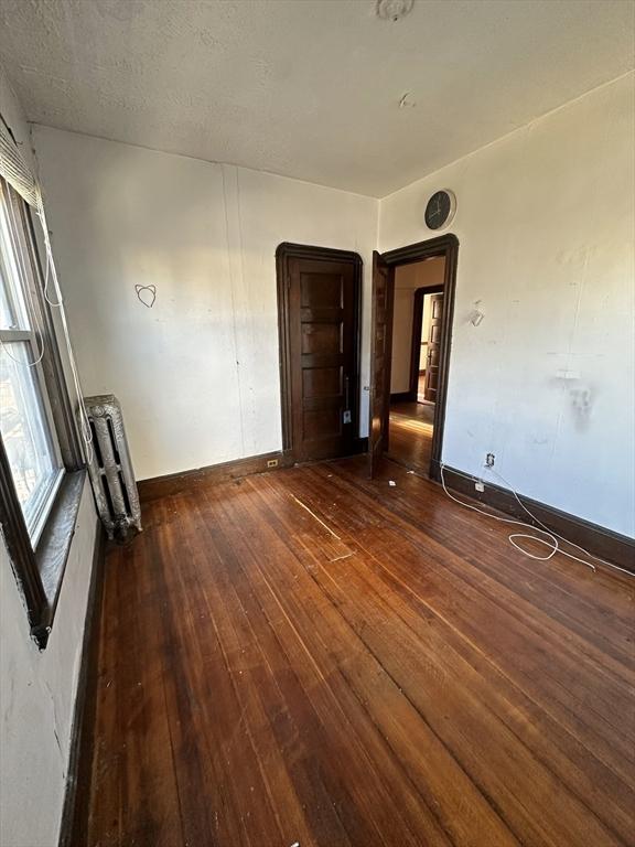 empty room featuring baseboards, dark wood-type flooring, and radiator