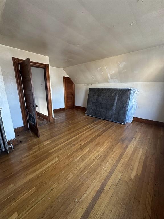 bonus room with dark wood-style floors, lofted ceiling, and baseboards