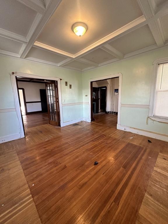 unfurnished room featuring beamed ceiling, coffered ceiling, dark wood-type flooring, and wainscoting