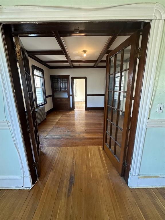 hall with radiator heating unit, dark wood-type flooring, coffered ceiling, beamed ceiling, and baseboards