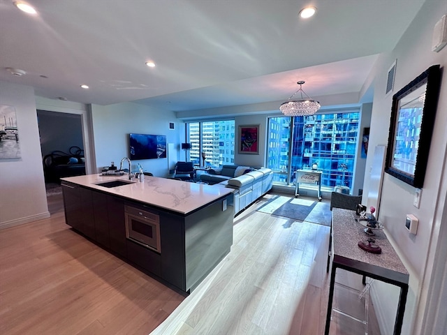 kitchen with sink, a chandelier, pendant lighting, a kitchen island with sink, and light wood-type flooring