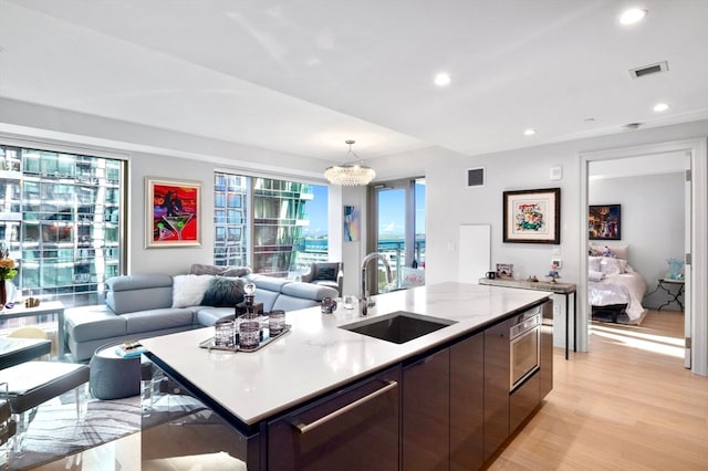 kitchen with sink, light hardwood / wood-style flooring, a notable chandelier, decorative light fixtures, and a center island with sink