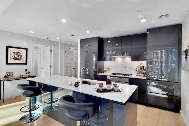 kitchen with light hardwood / wood-style floors, a kitchen bar, sink, and stainless steel gas cooktop