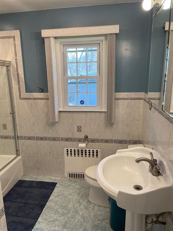 full bath featuring a sink, tile walls, radiator, toilet, and shower / bath combination with glass door