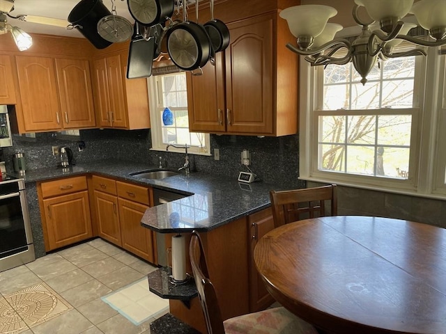 kitchen featuring a sink, backsplash, appliances with stainless steel finishes, brown cabinets, and light tile patterned floors
