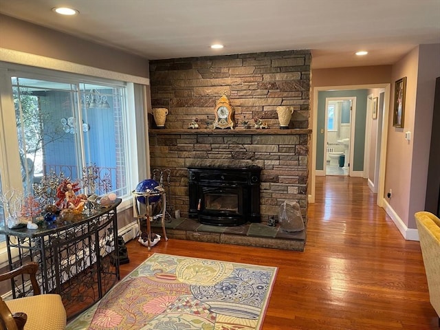 living area featuring baseboard heating, a stone fireplace, wood finished floors, baseboards, and recessed lighting