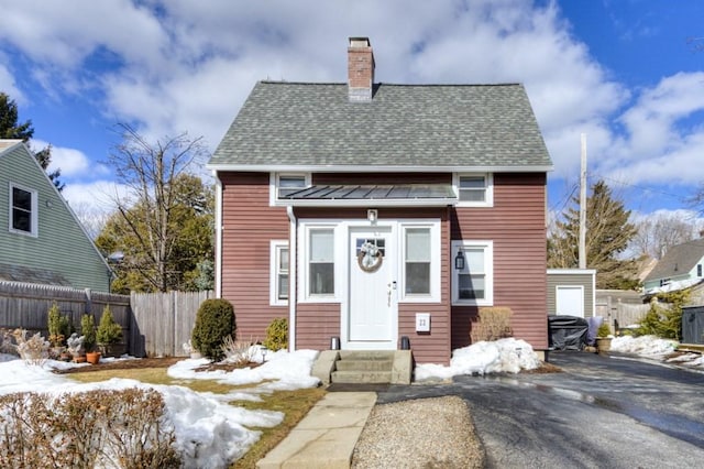 view of front of house with a chimney, fence, and roof with shingles