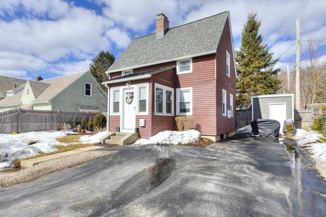 view of front facade featuring entry steps, a shingled roof, a chimney, and fence