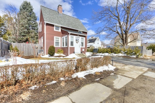 view of front of house featuring entry steps, a shingled roof, a chimney, and fence