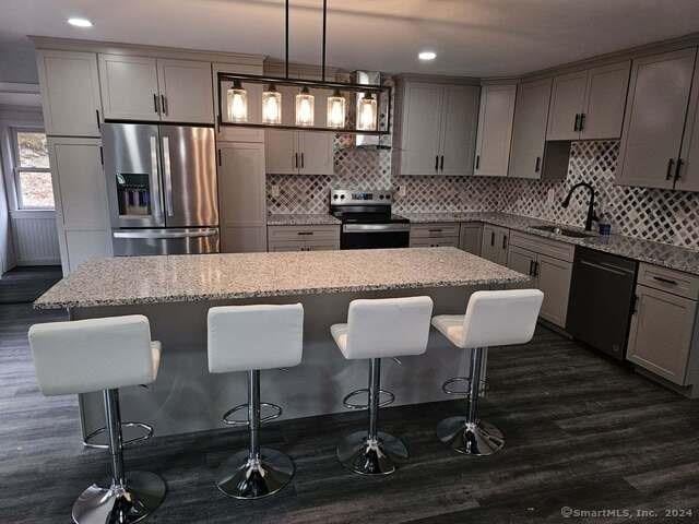 kitchen with light stone countertops, sink, a kitchen island, decorative light fixtures, and stainless steel appliances