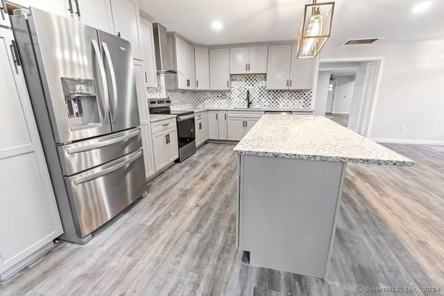 kitchen with light hardwood / wood-style flooring, decorative light fixtures, light stone countertops, a center island, and stainless steel appliances