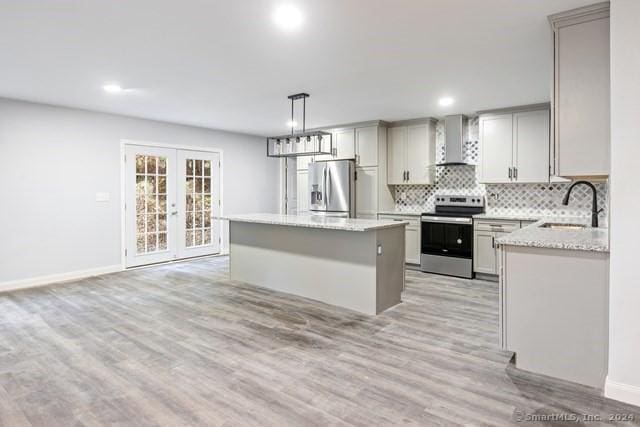 kitchen with appliances with stainless steel finishes, wall chimney range hood, a kitchen island, french doors, and pendant lighting