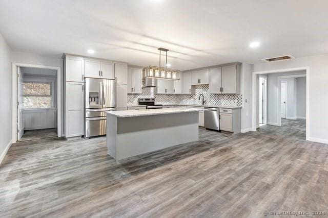 kitchen featuring pendant lighting, appliances with stainless steel finishes, a kitchen island, wood-type flooring, and gray cabinetry