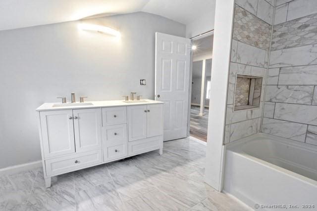 bathroom featuring vanity, vaulted ceiling, and tiled shower / bath