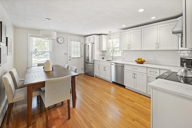 kitchen featuring white cabinets, stainless steel appliances, decorative backsplash, sink, and hanging light fixtures