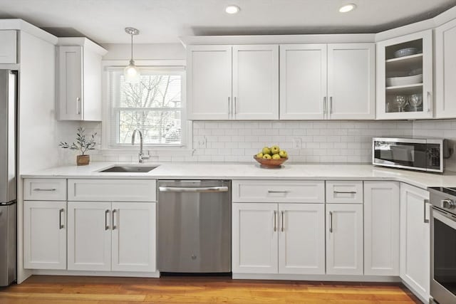 kitchen featuring white cabinets, appliances with stainless steel finishes, decorative light fixtures, sink, and light wood-type flooring