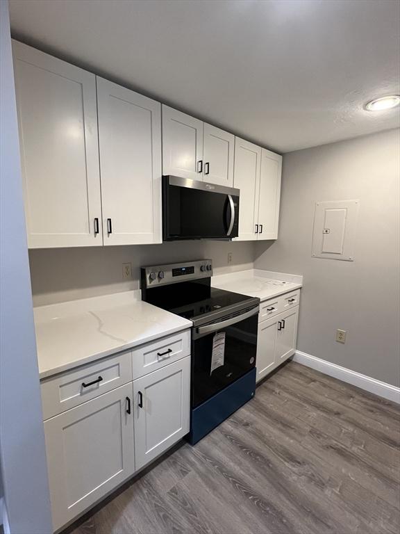 kitchen with white cabinets, light stone counters, dark wood finished floors, stainless steel appliances, and baseboards