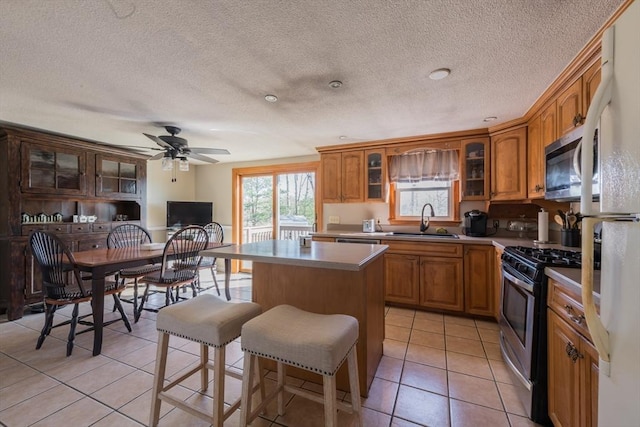 kitchen featuring stainless steel gas stove, a sink, a kitchen island, brown cabinetry, and light tile patterned floors