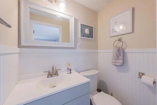 half bath featuring vanity, toilet, a wainscoted wall, and a textured ceiling