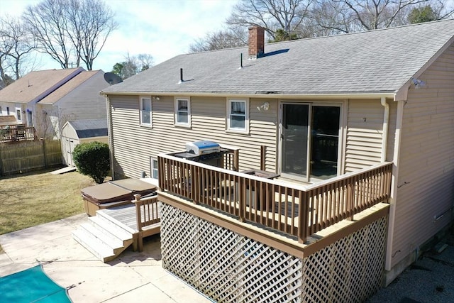 back of property featuring fence, a wooden deck, roof with shingles, a chimney, and a patio area