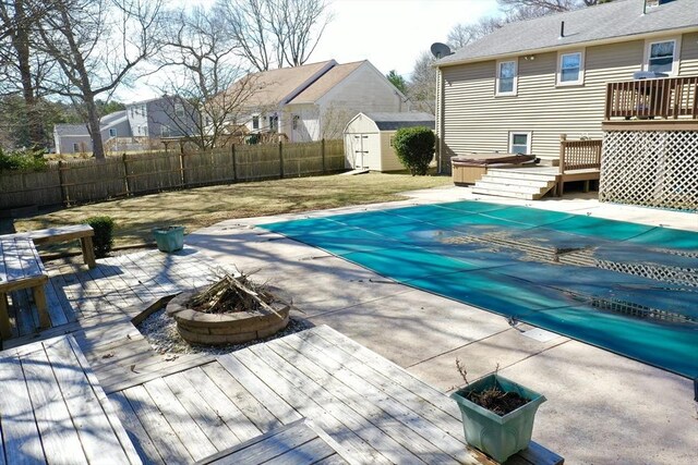 view of pool with an outdoor fire pit, a storage shed, a fenced backyard, a deck, and an outbuilding