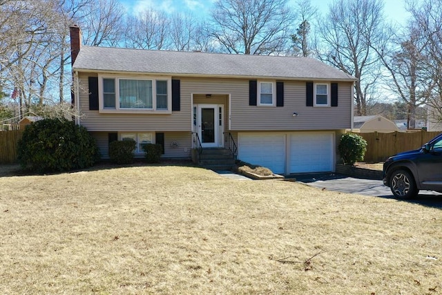 raised ranch featuring driveway, fence, a front yard, an attached garage, and a chimney