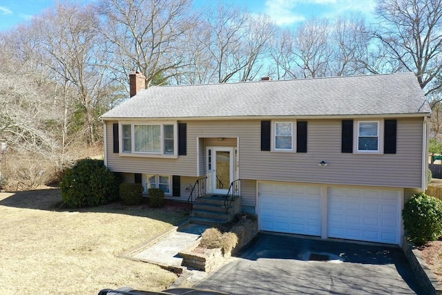 split foyer home featuring roof with shingles, an attached garage, driveway, and a chimney