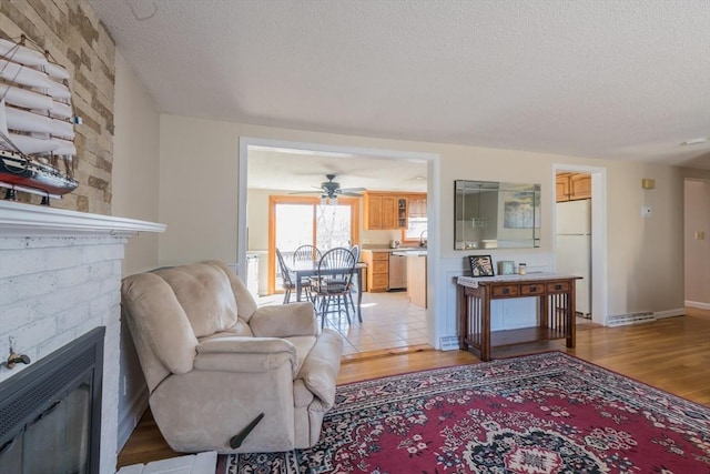 living area with a brick fireplace, light wood finished floors, and a textured ceiling