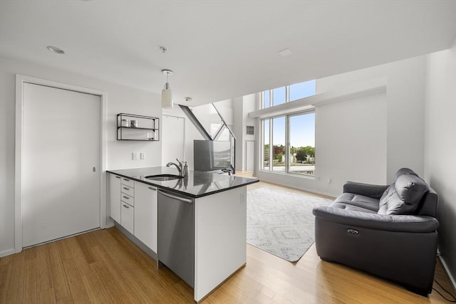 kitchen with open floor plan, a peninsula, stainless steel dishwasher, dark countertops, and a sink