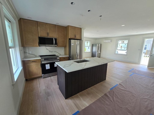 9 Swan St, Beverly, MA 01915 - kitchen featuring appliances with stainless steel finishes, light wood-type flooring, brown cabinetry, a center island with sink, and light stone countertops