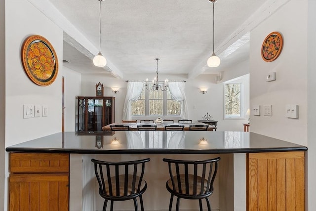 kitchen with brown cabinetry, dark countertops, a breakfast bar area, pendant lighting, and beam ceiling