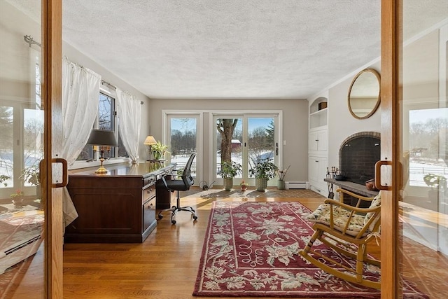 home office with light wood-type flooring, a baseboard radiator, and a textured ceiling