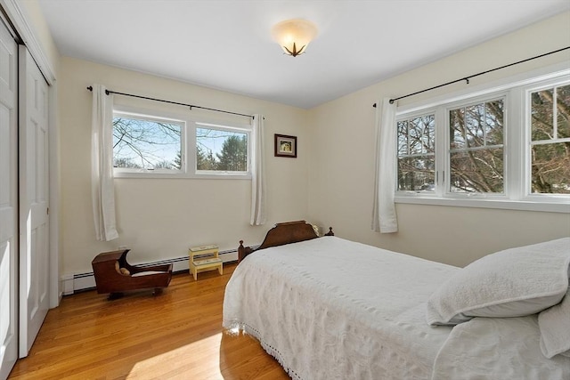 bedroom with light wood-type flooring, a closet, and a baseboard radiator