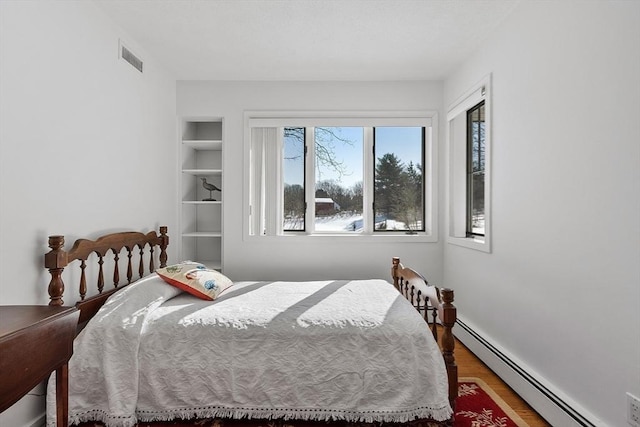 bedroom featuring a baseboard heating unit, wood finished floors, and visible vents