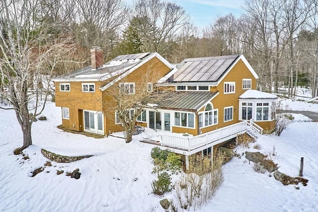 snow covered back of property featuring metal roof, a sunroom, roof mounted solar panels, a standing seam roof, and a chimney